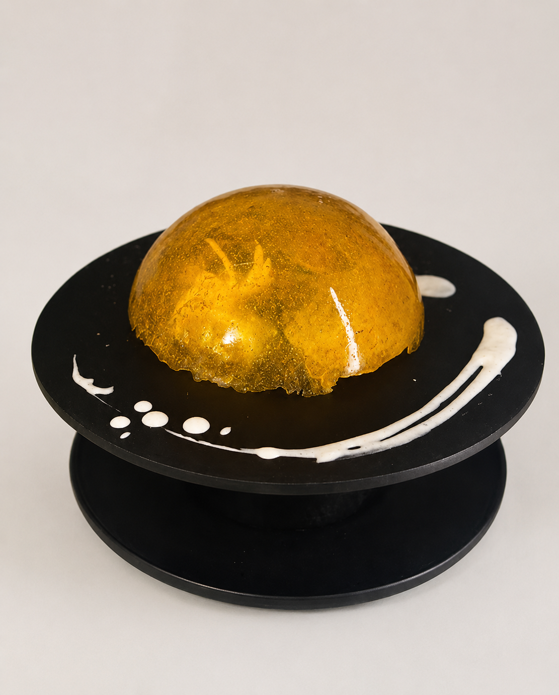 Amber isomalt lid resting over a dessert on a black plate